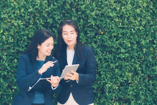 Two business people discussing information on a tablet-and taking notes as they work together as a team in the garden.