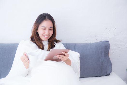 Asian woman lying in bedroom with digital tablet and drink coffee in morning lifestyle concept.