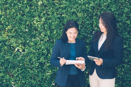 Two business people discussing information on a tablet-and taking notes as they work together as a team in the garden.