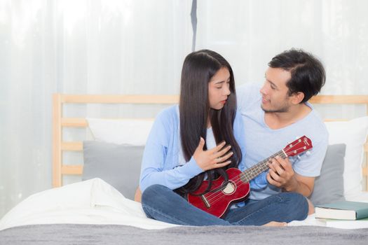 Young Asian couple playing ukulele relaxing with happiness and joyful in bedroom.