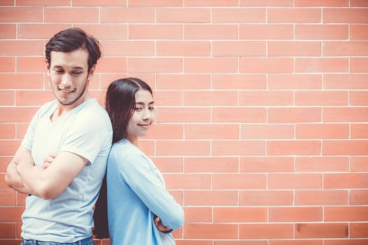 Young couple asian attractive looking face and smiling while standing back to back against brick wall with romantic.
