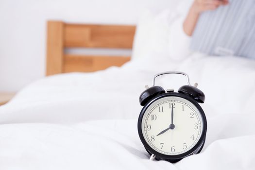 Beautiful asian woman laying and reading book in bed sleep behind alarm clock, time concept.