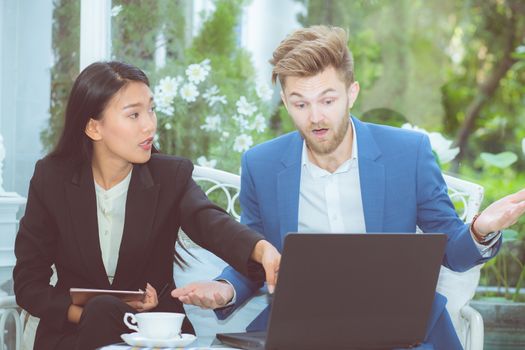 Two business man and woman with laptop - tablet pc computer and papers having discussion in office.