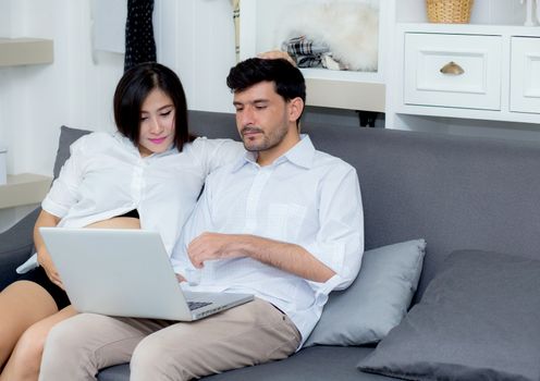 Portrait of a asian young couple husband and wife sitting on the sofa while using notebook computer in living room.