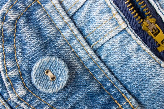 Jeans button bottom left corner with part of pocket and zip on pale blue jeans fabric. Jeans style for fashion design.