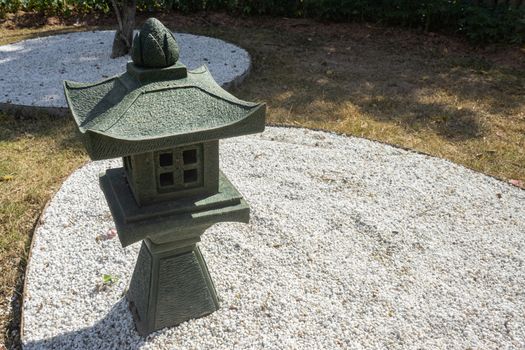 Stone or Rock Japanese Pagoda Lantern in Garden with Small White Rock on Ground on Left Frame with Natural Light