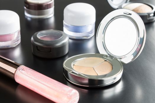 Woman cosmetics include lip gloss and eyeshadow and foundation or face powder on black Floor