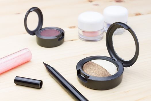 Woman cosmetics include eyes liner and lip gloss, and eyeshadow on wood table
