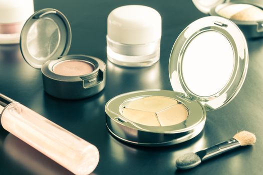 Woman cosmetics include lip gloss and eyeshadow and foundation or face powder and brush on black floor vintage style