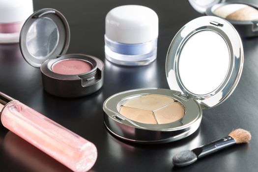 Woman cosmetics include lip gloss and eyeshadow and foundation or face powder and brush on black floor
