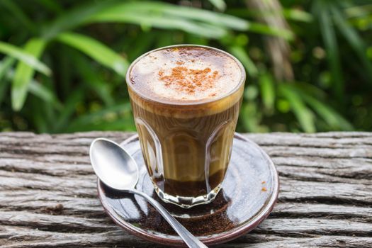 Latte Coffee in Glass with Spoon on Wood Table on Natural Green Tree Background. Latte coffee in coffee shop or cafe
 with nature green tree 
relax emotion background