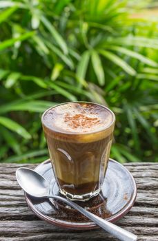 Latte Coffee in Glass with Spoon on Wood Table on Natural Green Tree Background Portrait. Latte coffee in coffee shop or cafe
 with nature green tree 
relax emotion background