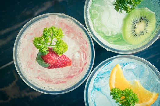 Red Green Blue Italian Soda Cold Beverage and Strawberry Kiwi Lemon Fruit and Parsley. Red Green Blue Italian Soda Cold Beverage on wood table for food and drink category