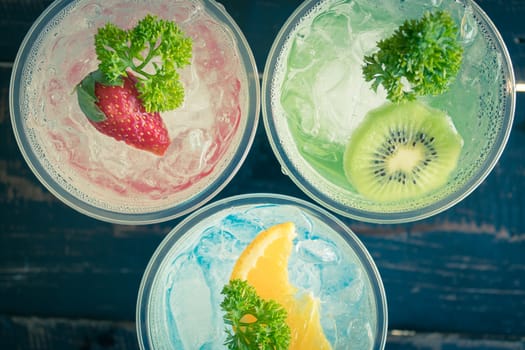 Green Blue Red Italian Soda Cold Beverage and Kiwi Lemon Strawberry Fruit and Parsley. Green Blue Red Italian Soda Cold Beverage on wood table for food and drink category
