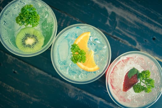 Green Blue Red Italian Soda Cold Beverage and Kiwi Lemon Strawberry Fruit and Parsley. Green Blue Red Italian Soda Cold Beverage on wood table for food and drink category