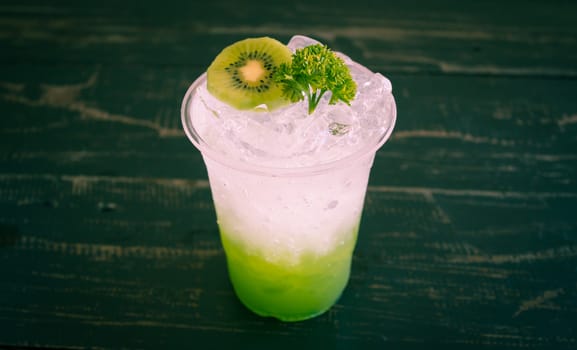 Green Italian Soda Cold Beverage and Kiwi Fruit and Parsley Center. Green Italian Soda Cold Beverage with Kiwi fruit and ice in glass on wood table for food and drink category