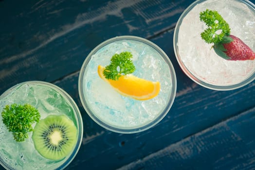 Green Blue Red Italian Soda Cold Beverage and Kiwi Lemon Strawberry Fruit and Parsley. Green Blue Red Italian Soda Cold Beverage on wood table for food and drink category