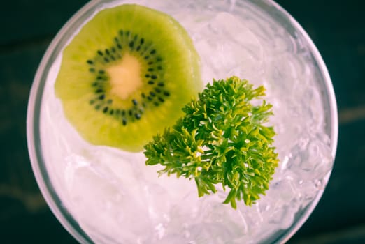 Green Italian Soda Cold Beverage and Kiwi Fruit and Parsley. Green Italian Soda Cold Beverage with Kiwi fruit and ice in glass on wood table. Green Italian Soda with Kiwi for food 
and drink category