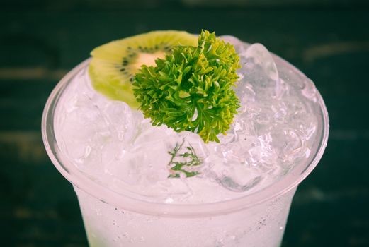 Green Italian Soda Cold Beverage and Kiwi Fruit and Parsley. Green Italian Soda Cold Beverage with Kiwi fruit and ice in glass on wood table. Green Italian Soda with Kiwi for food 
and drink category