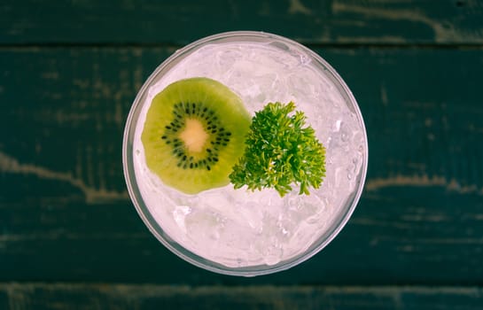 Green Italian Soda Cold Beverage and Kiwi Fruit and Parsley. Green Italian Soda Cold Beverage with Kiwi fruit and ice in glass on wood table. Green Italian Soda with Kiwi for food 
and drink category