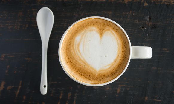 Heart Shape Froth Milk Latte Art in White Coffee Cup and Spoon on Black Wood Table. Heart shape froth milk Latte art hot beverage for coffee lover