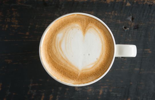 Heart Shape Froth Milk Latte Art in White Coffee Cup on Black Wood Table. Heart shape froth milk Latte art hot beverage for coffee lover