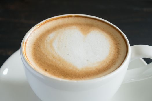 Heart Shape Froth Milk Latte Art in White Coffee Cup Zoom on Black Wood Table. Heart shape froth milk Latte art hot beverage for coffee lover