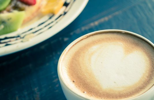 Vintage Heart Shape Froth Milk Latte Art in White Coffee Cup with Dessert on Black Wood Table. Heart shape froth milk Latte art hot beverage for coffee lover