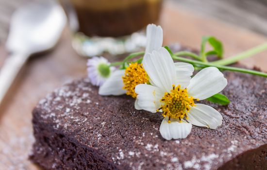 Daisy Flower on Chocolate Brownie Cake with Latte Coffee and Spoon on Chopping Board or Cutting Board on Wood Table Right Close Up. Relax coffee break time in 
coffee shop right frame