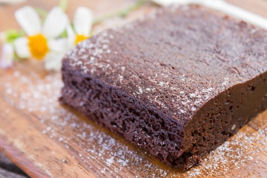 Chocolate Brownie Cake and Daisy Flower and Spoon on Chopping Board or Cutting board on Wood Table in Close Up angle