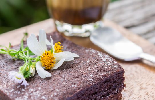 Daisy Flower on Chocolate Brownie Cake with Latte Coffee and Spoon on Wood Table Left Close Up. Relax coffee break time in coffee shop left frame