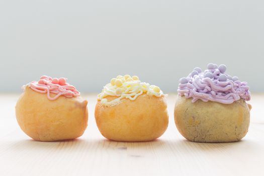 3 Color of choux pastry or cream puff or profiterole that have whipped cream on the head. Eclair dessert on wood table in horizontal view.