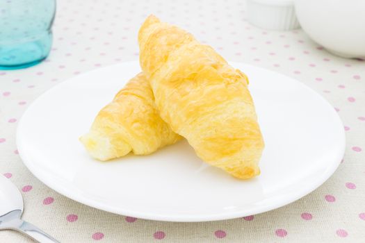 Croissant or bread or bakery on white dish on pink point placemat with spoon and tea cup and glass