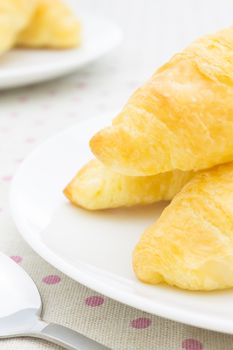 Croissant or bread or bakery on white dish on pink point placemat with spoon close up view