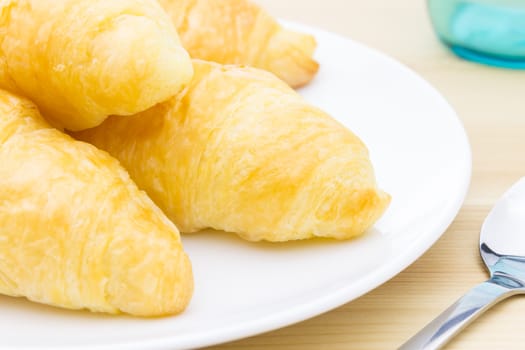 Croissant or bread or bakery on white dish on wood table and glass and spoon close up view