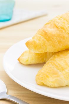 Croissant or bread or bakery on white dish on wood table with spoon and glass and napkin portrait view