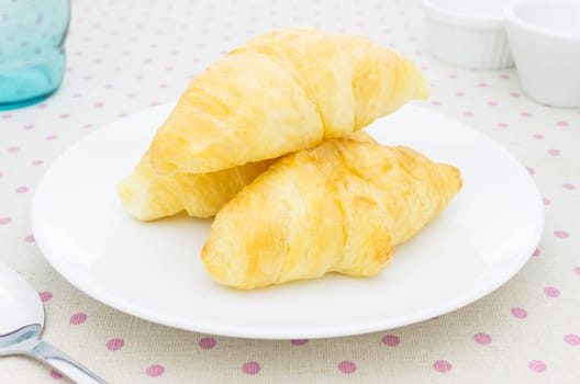 Croissant or bakery or bread on white dish on pink point placemat with Green Glass and tea cup