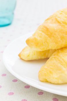 Croissant or bread or bakery on white dish on pink point placemat with glass close up view