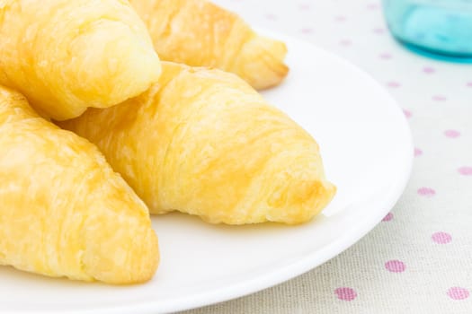 Croissant or bread or bakery on white dish on pink point placemat with glass close up view