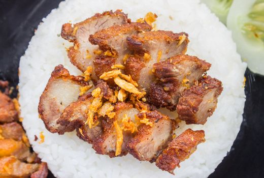 Thai Food Fried Pork with Garlic and Cucumber in Black Dish Top view Zoom. Fried pork with garlic or steak on rice and cucumber in food and drink category flatray or top table view zoom