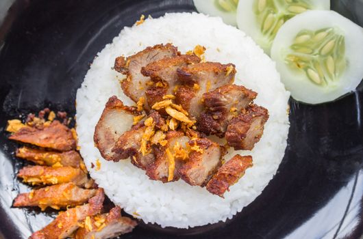 Thai Food Fried Pork with Garlic and Cucumber in Black Dish Top view. Fried pork with garlic or steak on rice and cucumber in food and drink category flatray or top table 
view