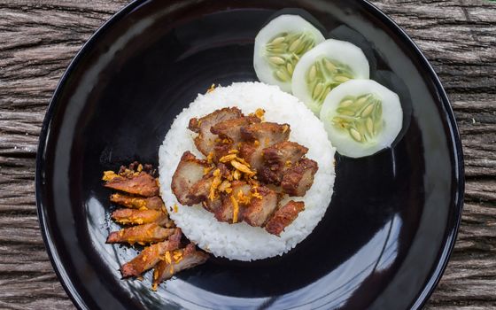 Thai Food Fried Pork with Garlic and Cucumber in Black Dish Top view Wide. Fried pork with garlic or steak on rice and cucumber in food and drink category flatray or top table view zoom