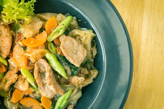 Stir Fried Noodle and Pork and Carrot and Yardlong Beans and Lettuce with Black Soy Sauce on Top View with Natural Light on Left Frame in Vintage Tone