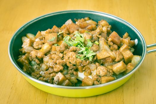 Stir Fried Pork with Onion and Garlic and Black Soy Sauce and Coriander Topping and Tofu in Pan on Wood Table with Natural Light in Vintage Tone