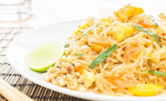 Pad Thai or Thai fried noodles on white dish and bamboo placemats. Chopsticks and glass and egg dry shrimps onions sprouts lemon peanut