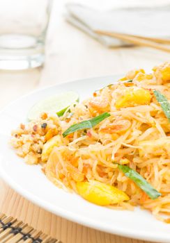 Pad Thai or Thai fried noodles on white dish on wood table vertical style. Glass and napkin chopsticks egg dry shrimps onions sprouts lemon peanut