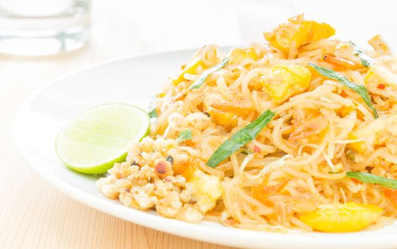 Pad Thai or Thai fried noodles on white dish on wood table. Glass and egg dry shrimps onions sprouts lemon peanut