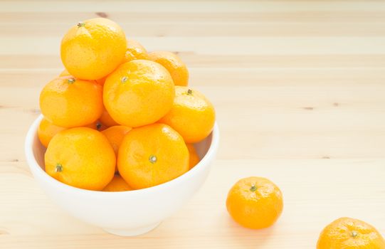 China orange or mandarin or tangerine or small orange in white bowl with two orange on wood table