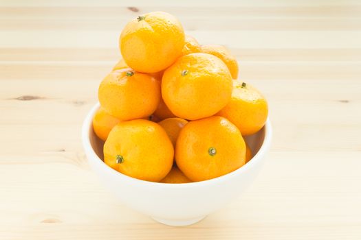 China orange or mandarin or tangerine or small orange in white bowl on wood table center of frame