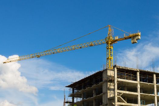 Yellow tower crane wide screen on blue sky background. Crane is building skyscraper in site.